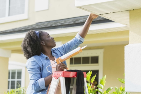 woman applying sealant on gutter